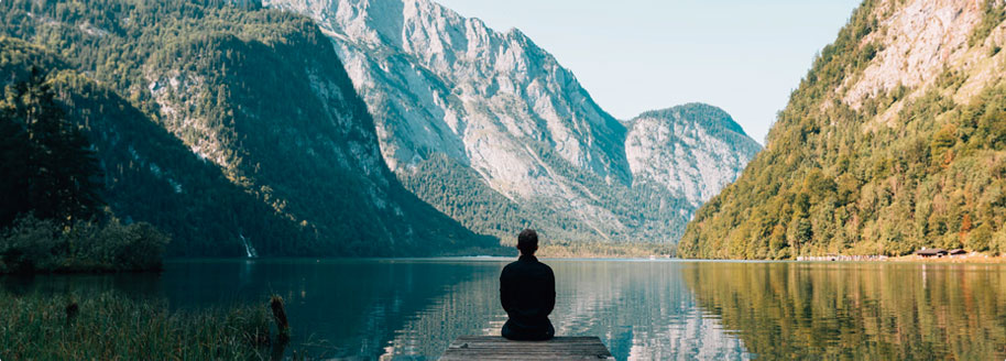 Silhouetted figure sitting on the end of a dock facing mountain scenery